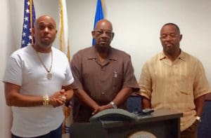 Festival President David Charlemagne, left, addresses the Festival Village reopening with Police Commissioner Delroy Richards and Franklin Johnson.