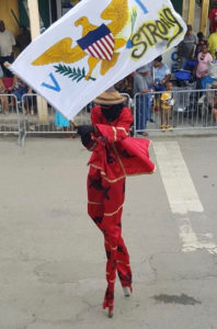 A moko jumbie waves a 'V.I. Strong' banner while marching Saturday. (Photo by Jess Parker)