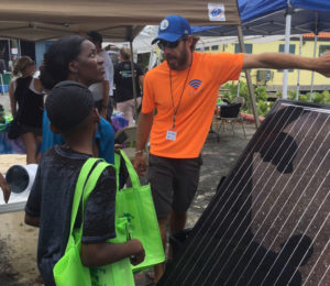 Pete Mottl explains how a solar panel creates electricity to Thora Henry Letang and her children.