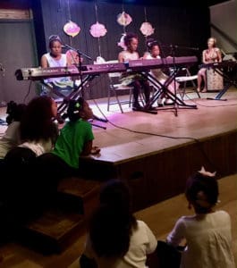 Young audience members cluster around the stage to give their full attention to piano students.