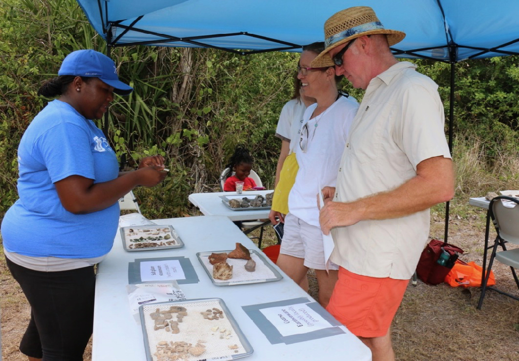 Alicia Olewale, assistant professor of anthropology at the University of Tulsa, interprets one of the artifacts on display at Little Princess to Jeffrey Miller and Jennifer Miller. (Source photo by Linda Morland)