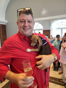 Jim Hines, General Manager at Bellows International, smiles while holding a puppy in one arm and a glass in the other. (Photo submitted by Annette Zachman)