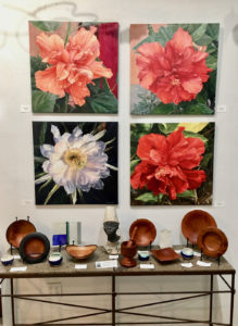 Karen’s floral paintings hang above Avelino’s carving at Bajo El Sol Gallery. (Source photo by Amy Roberts)