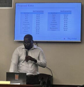 PSC hearing examiner Jed JohnHope stands in front of a graphic listing proposed fees. (Source photo by Amy H. Roberts)